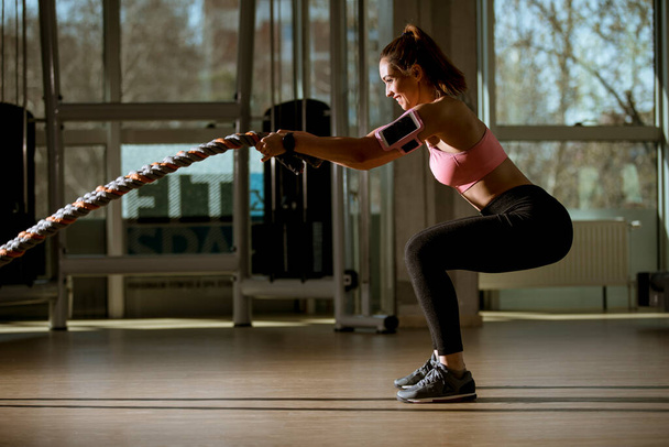 Hübsche junge Frau mit Kampfseilen turnt im Fitnessstudio - Foto, Bild