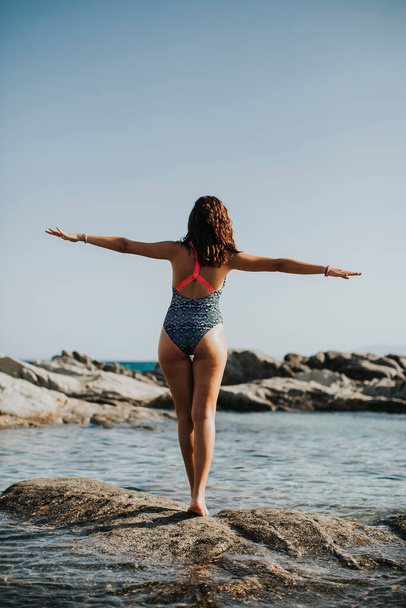 Mujer joven y bonita en bikini caminando sobre rocas junto al mar
 - Foto, Imagen