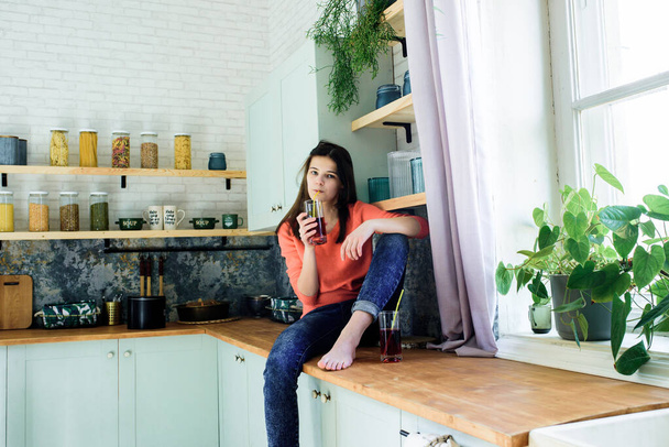 Modern lifestyle.Happy slim teenage girl in the kitchen with a glass of natural juice. Red juice of cherry or strawberry. Natural healthy nutrition, fresh vegetables - 写真・画像