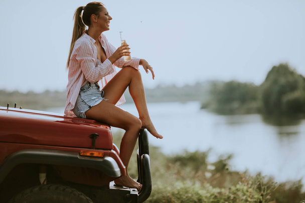 Piękne młode kobiety pijące jabłecznik w samochodzie nad jeziorem. - Zdjęcie, obraz