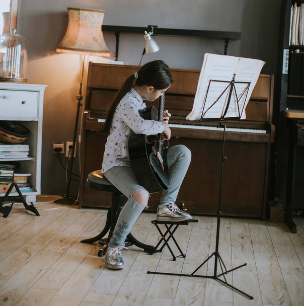 Cute little girl practicing on a acoustic guitar at rustic home - Foto, afbeelding