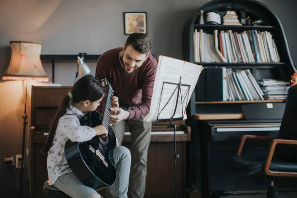 Cute little girl playing guitar with her music teacher in the rustic apartment - Foto, imagen