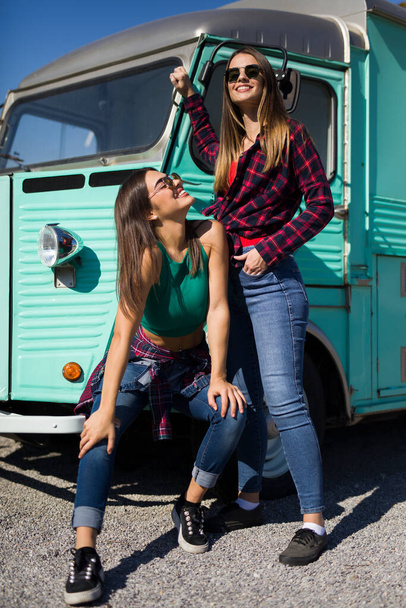 Two smiling pretty young women by the vintage minivan - Photo, Image