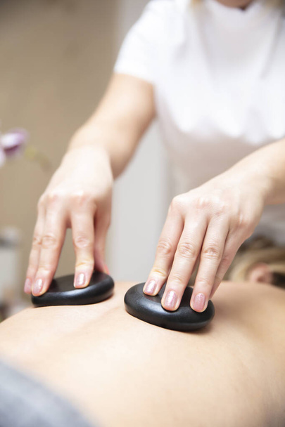 Masážní terapeut pomocí horkých lávových kamenů na beck mladé ženy během lázeňské relaxační kamenné terapie - Fotografie, Obrázek