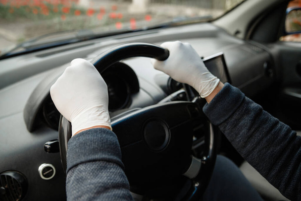 Mężczyzna prowadzący samochód w ochronnej masce medycznej i rękawiczkach. Bezpieczna jazda taksówką podczas pandemii koronawirusa. Ochrona kierowcy i pasażerów przed bakteriami i zakażeniem wirusem podczas kwarantanny - Zdjęcie, obraz