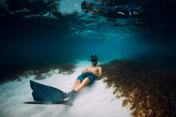 Freediver hombre con aletas liberadoras relajarse sobre fondo arenoso en el océano azul
 - Foto, imagen