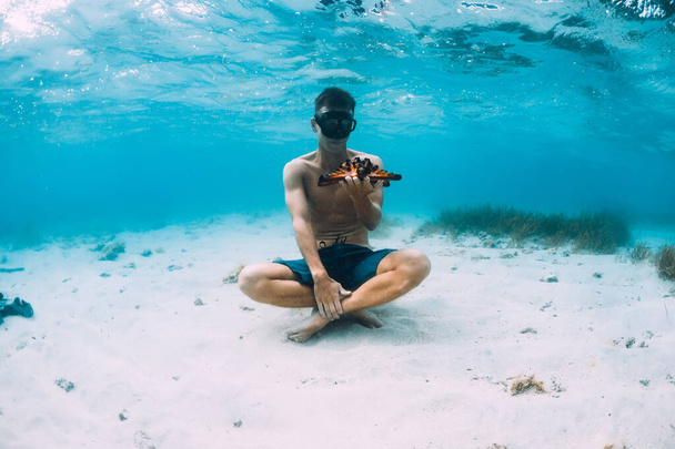 Freediver muž s držet hvězdice a relaxovat přes písčité dno v modrém oceánu - Fotografie, Obrázek
