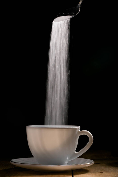 Azúcar granulado blanco vertiendo en una taza blanca
.  - Foto, Imagen