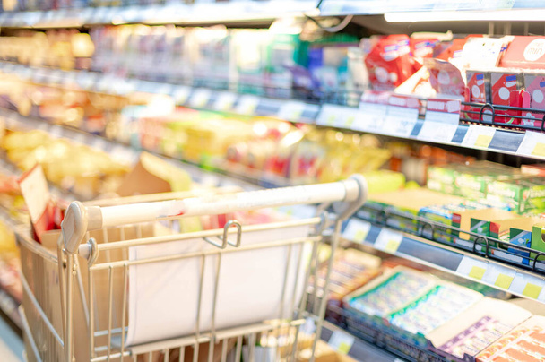 Efecto borroso en el pasillo del supermercado con carro de compras plateado y verde, Shopper eligiendo la comida en el supermercado Comprador de pánico para acaparar alimentos, concepto Coronavirus Covid-19
. - Foto, imagen