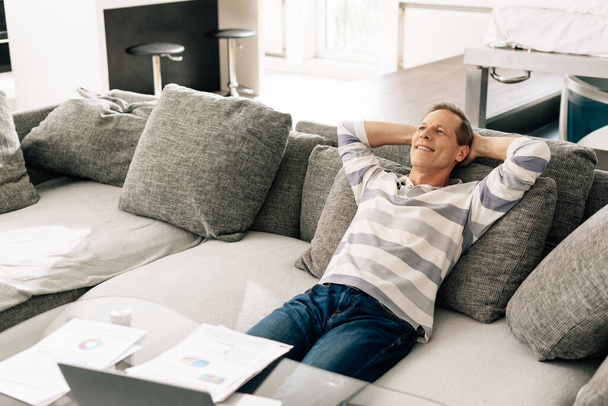 веселий чоловік розслабляється на дивані біля графіків і графіків на кавовому столі
  - Фото, зображення