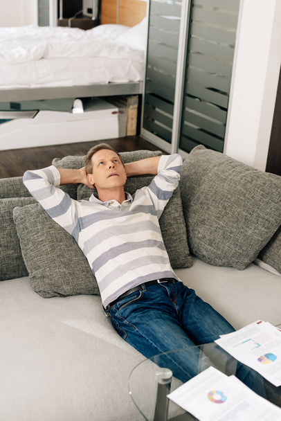 man relaxing on sofa near charts and graphs on coffee table  - Foto, Imagem
