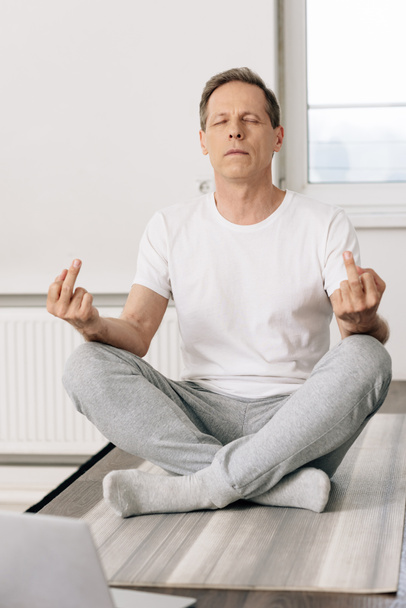 Mann in Socken sitzt in Lotus-Pose und zeigt Mittelfinger  - Foto, Bild