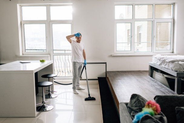 掃除機付きの疲れた男のクリーニングアパートの選択的な焦点  - 写真・画像
