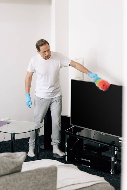 selective focus of man holding duster brush while cleaning blank tv screen in living room  - Photo, Image
