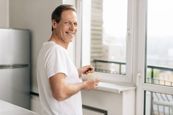 fröhlicher Mann mit Löffel mit Cornflakes und Schüssel zu Hause - Foto, Bild