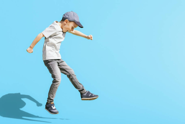 Young boy runs in the jump on the street on a bright blue background - Foto, afbeelding