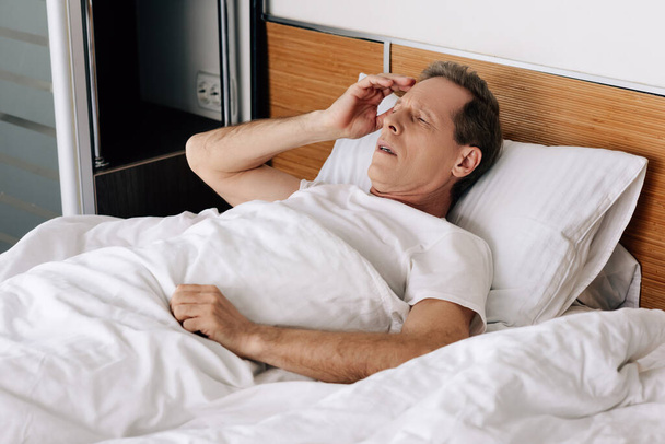 sick man lying on bed and touching head  - Fotó, kép