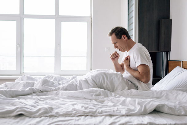 病気の男性が家のベッドで咳をしている姿を  - 写真・画像