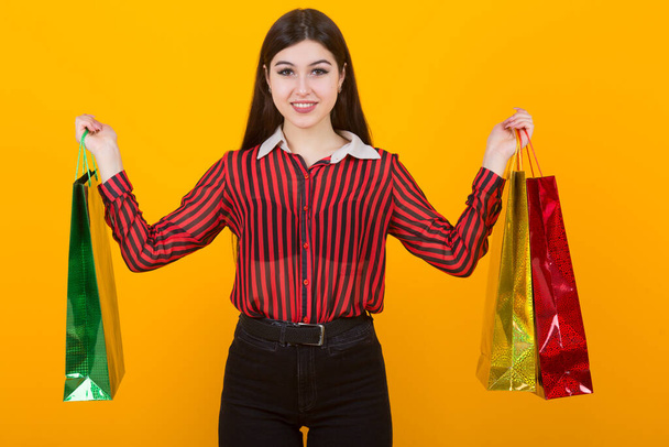beautiful young woman with packages in hands on a yellow background - 写真・画像