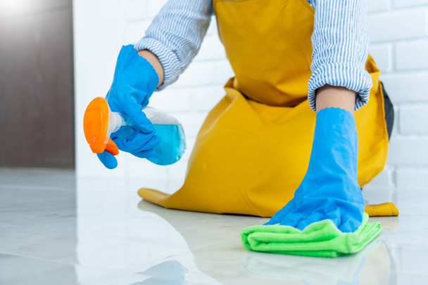 Housekeeper maid wearing rubber gloves with cloth cleaning or applying floor care and cleaners at home, housework and housekeeping concept - Fotó, kép