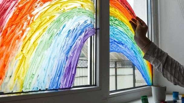 mão arco-íris pintura em uma janela, ficar em casa durante a quarentena, Imagem das crianças lazer em casa, Perseguir o flashmob arco-íris
 - Foto, Imagem