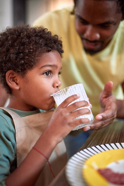 afrikkalainen isä auttaa poikaansa juomaan lasin maitoa. terveellinen, ruoka, perheen käsite
 - Valokuva, kuva