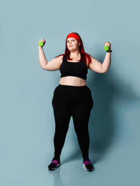 Big size plus overweight woman does exercises working out with small green weights dumbbells dieting standing full body - Foto, afbeelding