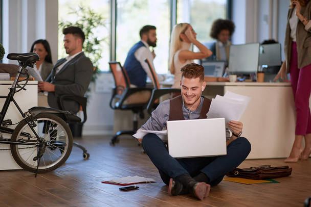 young business man looking at papers on his lap, satisfied, sitting on a floor in office. casual business concept - Foto, imagen