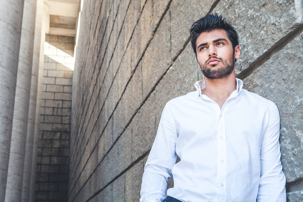 Young man outdoors with free space near. White shirt, fashionable hair and beard. The handsome guy is near a historic building with a dead end. - Фото, изображение