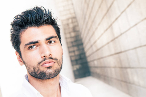 Beautiful young man with beard and stylish hair. Close portrait. Background with old brick building. - Photo, image