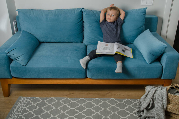 Boy reading book on sofa - Фото, изображение
