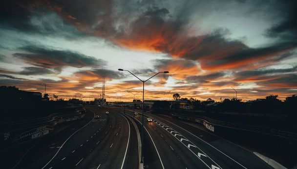 A landscape of the roads surrounded by trees under a cloudy sky during the breathtaking sunset - Foto, Imagem