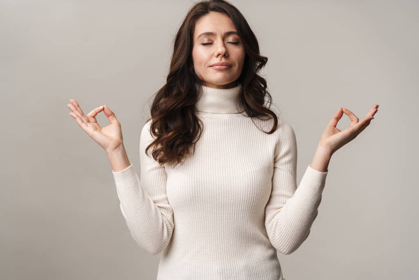 Photo of caucasian beautiful woman with long brown hair meditating and gesturing fingers isolated over beige background - Fotografie, Obrázek