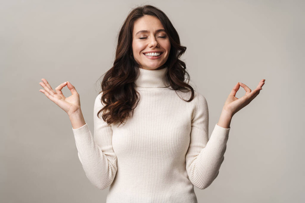 Photo of caucasian beautiful woman with long brown hair meditating and gesturing fingers isolated over beige background - Φωτογραφία, εικόνα
