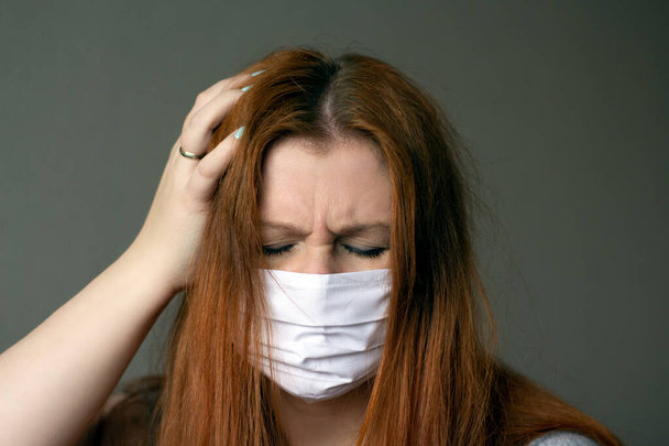 Red-haired young woman wearing respiratory medical mask holding a hand on her head and frowing because of headache .Coronavirus 2019-ncov covid-19 concept. - Φωτογραφία, εικόνα