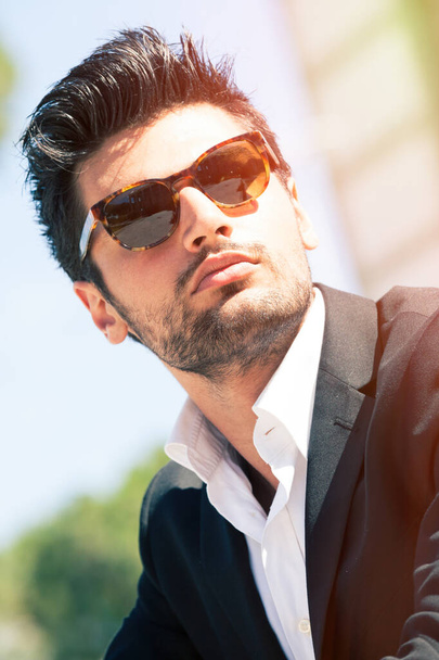 Gorgeous stylish man with sunglasses. Stubble and blacks hair. Intense light. White shirt and stylish jacket. - Foto, afbeelding