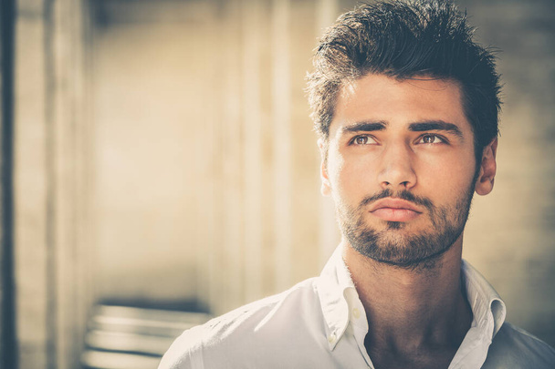 Handsome young man portrait. Intense look and eye-catching beauty. Fashionable hair and beard. The young man is wearing a white shirt. - Photo, Image