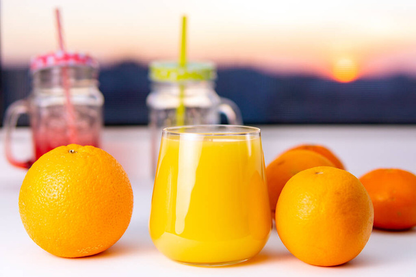 sklenice pomerančové šťávy a pomeranče, selektivní zaměření. při západu slunce, místo pro text, kopírovací prostor - Fotografie, Obrázek