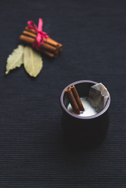 Чай с молоком с корицей, пакетик чая, черный чай, в коричневом чайнике на черном фоне
 - Фото, изображение