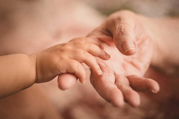 Die Hand eines kleinen Kindes greift nach der Hand einer älteren Frau - Foto, Bild