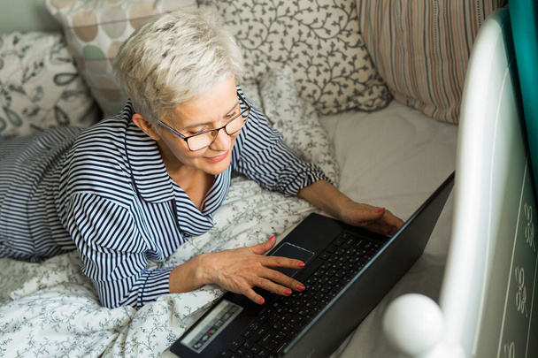 an elderly woman lies on a bed in pajamas - Zdjęcie, obraz