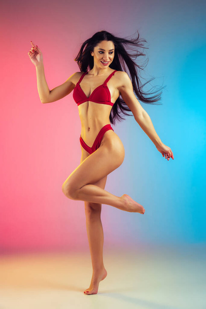 Fashion portrait of young fit and sportive woman in stylish red luxury swimwear on gradient background. Perfect body ready for summertime. - Φωτογραφία, εικόνα