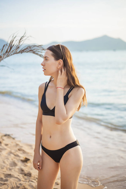 Beautiful woman in black bikini is relaxing on the beach, summer concept  - Фото, изображение