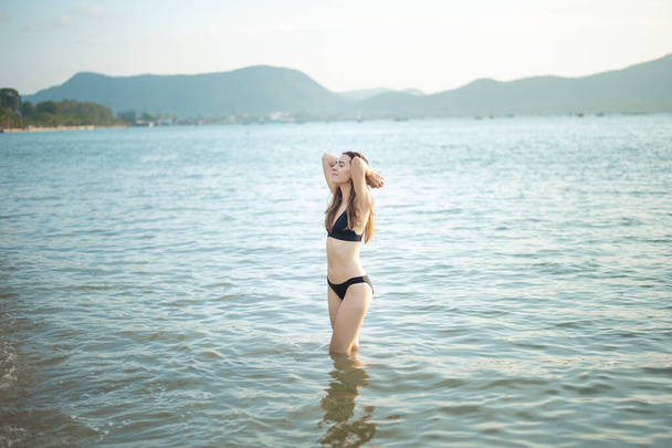 Beautiful woman in black bikini is enjoying with sea water on the beach  - Foto, imagen