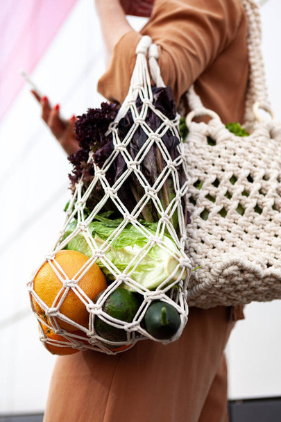 Mädchen hält eine Einkaufstasche mit Gemüse in der Hand, Grünzeug ohne Plastiktüten. Null Abfall, plastikfreies umweltfreundliches Konzept. Handgemachte Makramientasche. Nachhaltiger Lebensstil.   - Foto, Bild