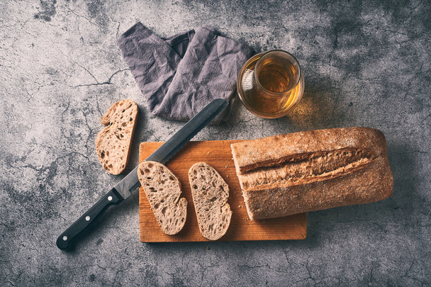Homemade bread cut on a wooden board together with a bottle of extra virgin olive oil. Traditional Mediterranean breakfast concept. - Photo, Image