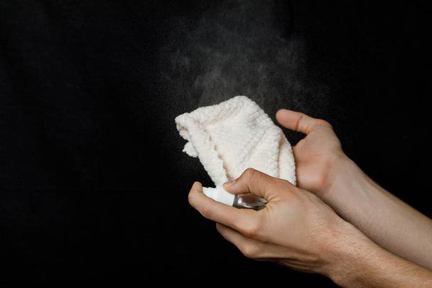 Hand sprüht Desinfektionsmittel auf einen Lappen auf schwarzem Hintergrund. - Foto, Bild