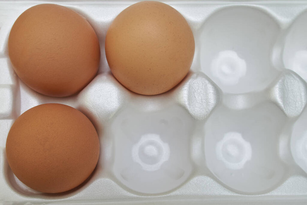 Huevos de pollo en una bandeja, bandeja de cartón vacía con tres huevos.
. - Foto, imagen