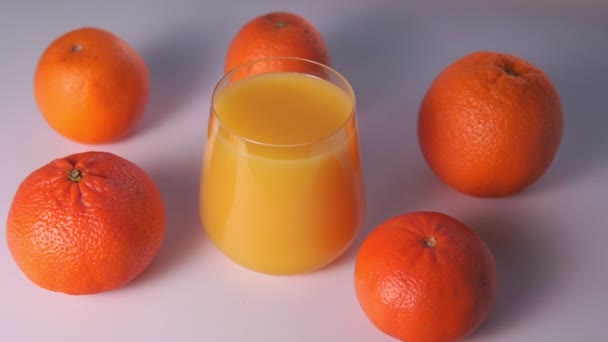 vidro de suco de laranja e frutas laranjas em um fundo branco, foco seletivo - Filmagem, Vídeo