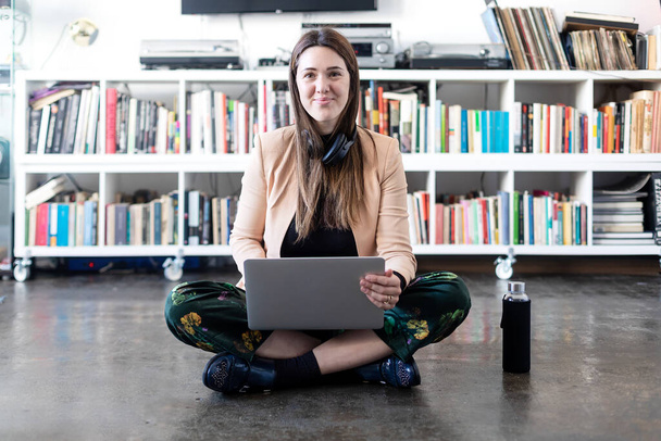 Junge hübsche Unternehmerin benutzt Laptop, während sie zu Hause auf dem Boden sitzt. - Foto, Bild